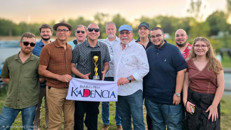 Kadencia Orchestra 2026 - The Cultural Current Twelve people posing outdoors, two in front holding a trophy and a Kadencia banner, celebrating a win.