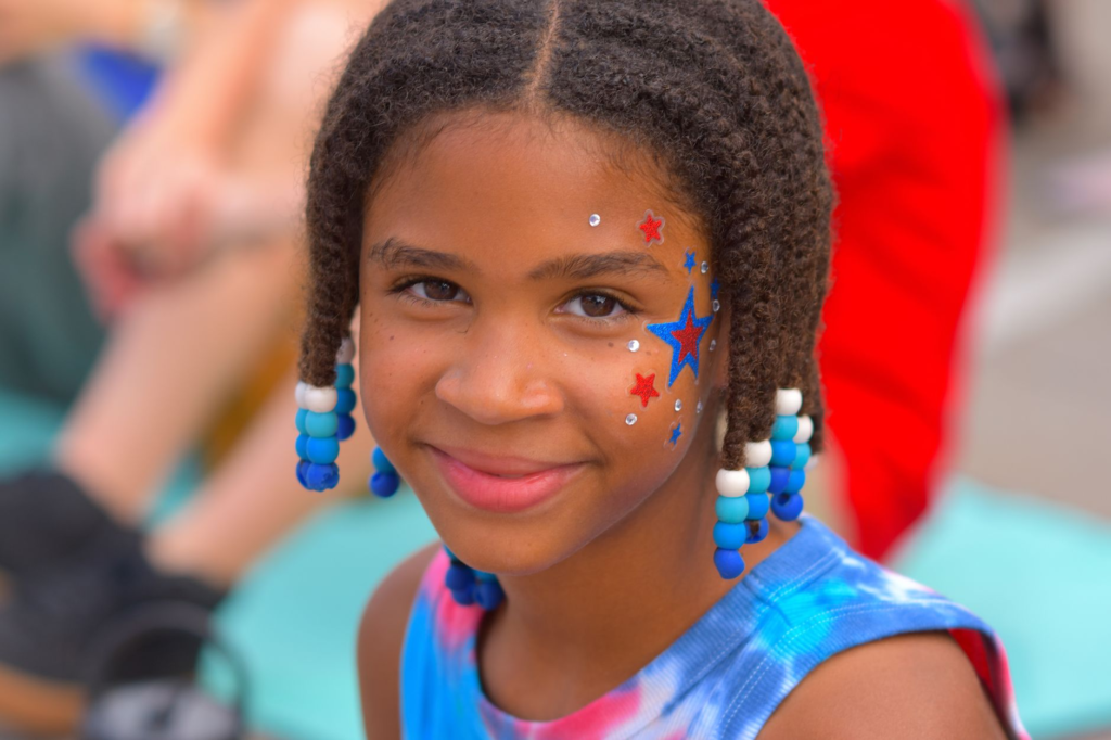 pexels-photo-38469083 - The Cultural Current cheerful girl with braided hair and face paint at outdoor event